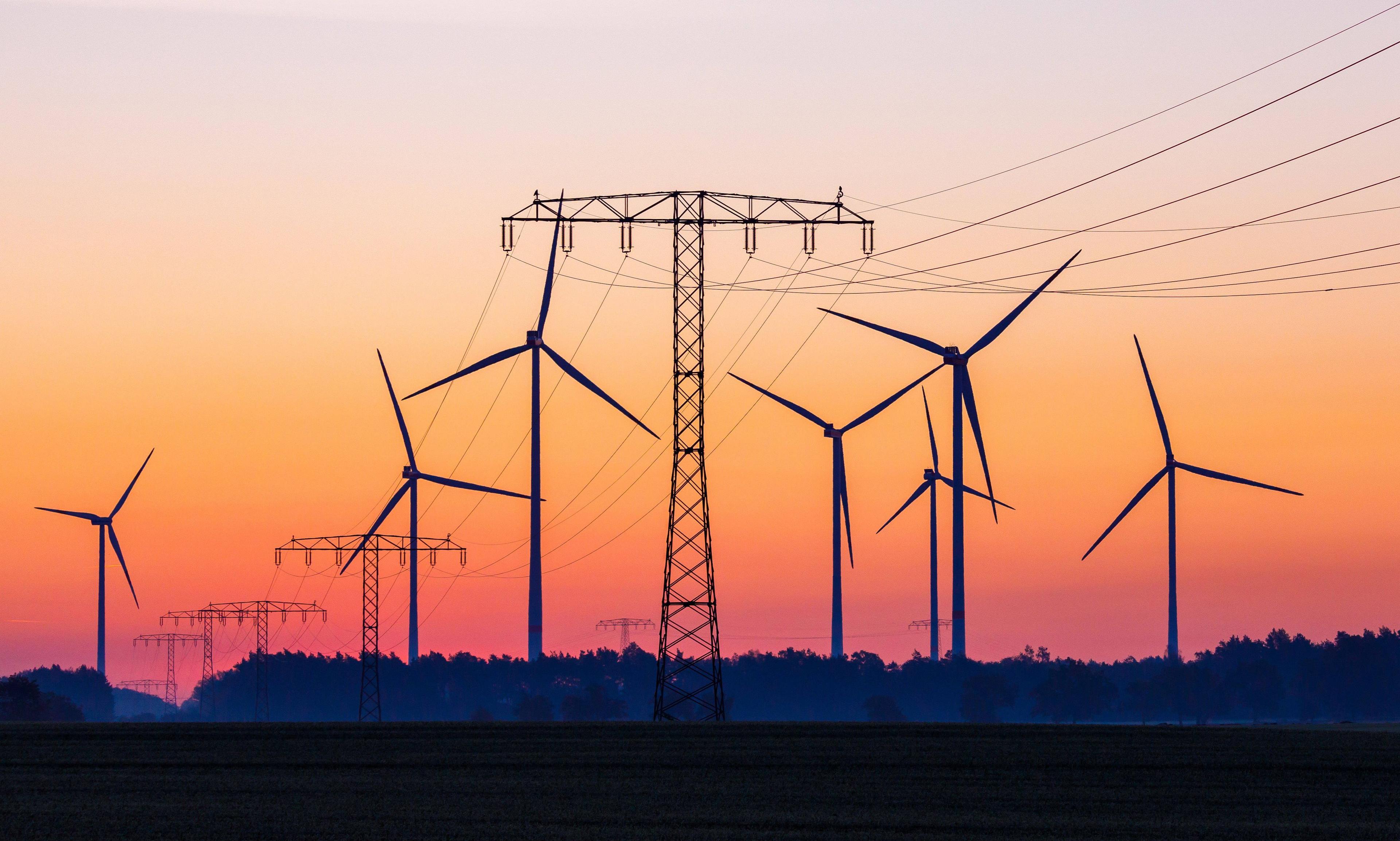 Ein Sonnenuntergang taucht diese Szenerie aus Strommasten und Windrädern in ein Spektrum von gelb bis lila – ganz zufällig die Farben von Deutsche Wohnen & Co. Enteignen.