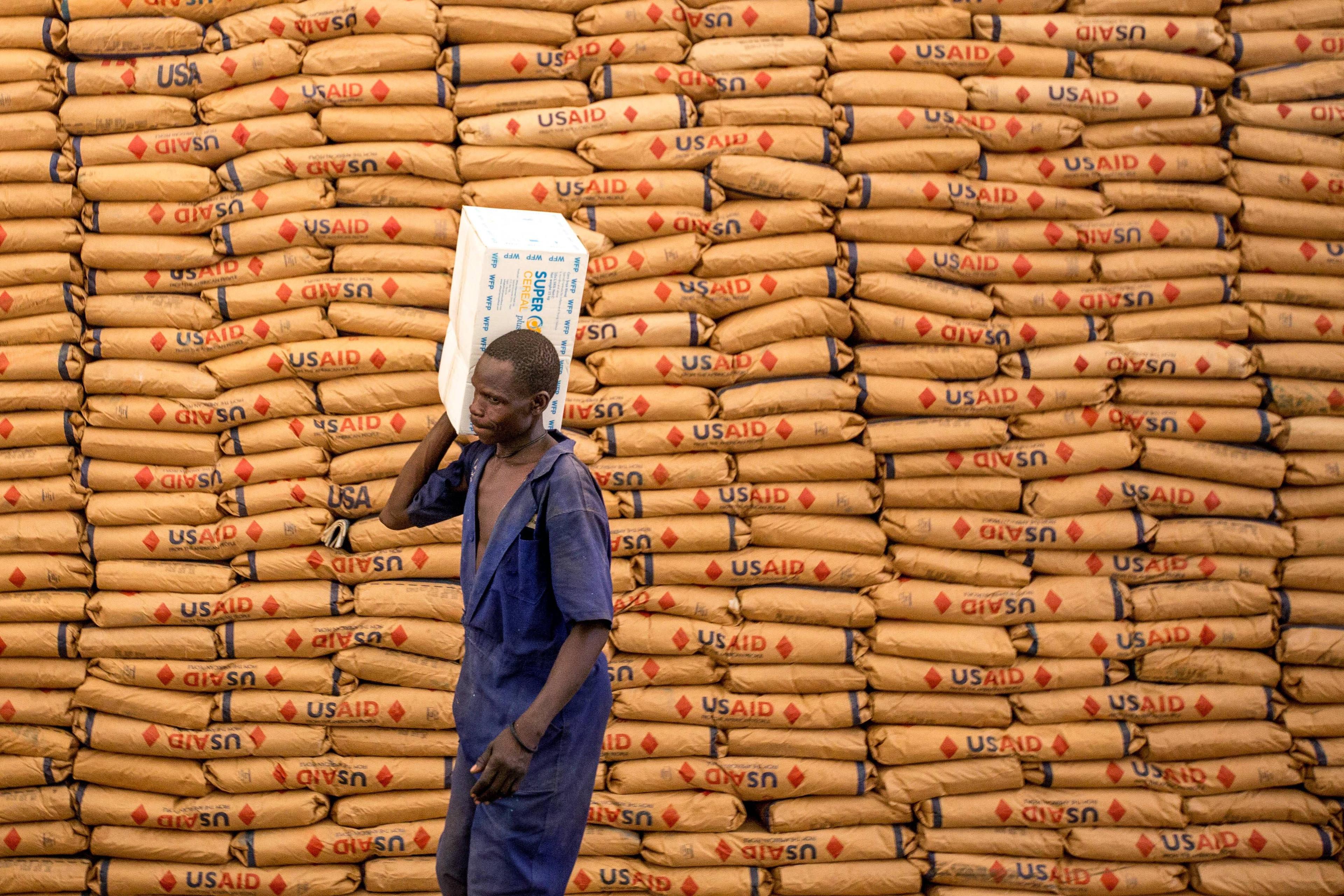 Geflüchteter aus dem Sudan in einem Aufnahmecamp in Uganda, im Hintergrund Getreidesäcke von USAID.