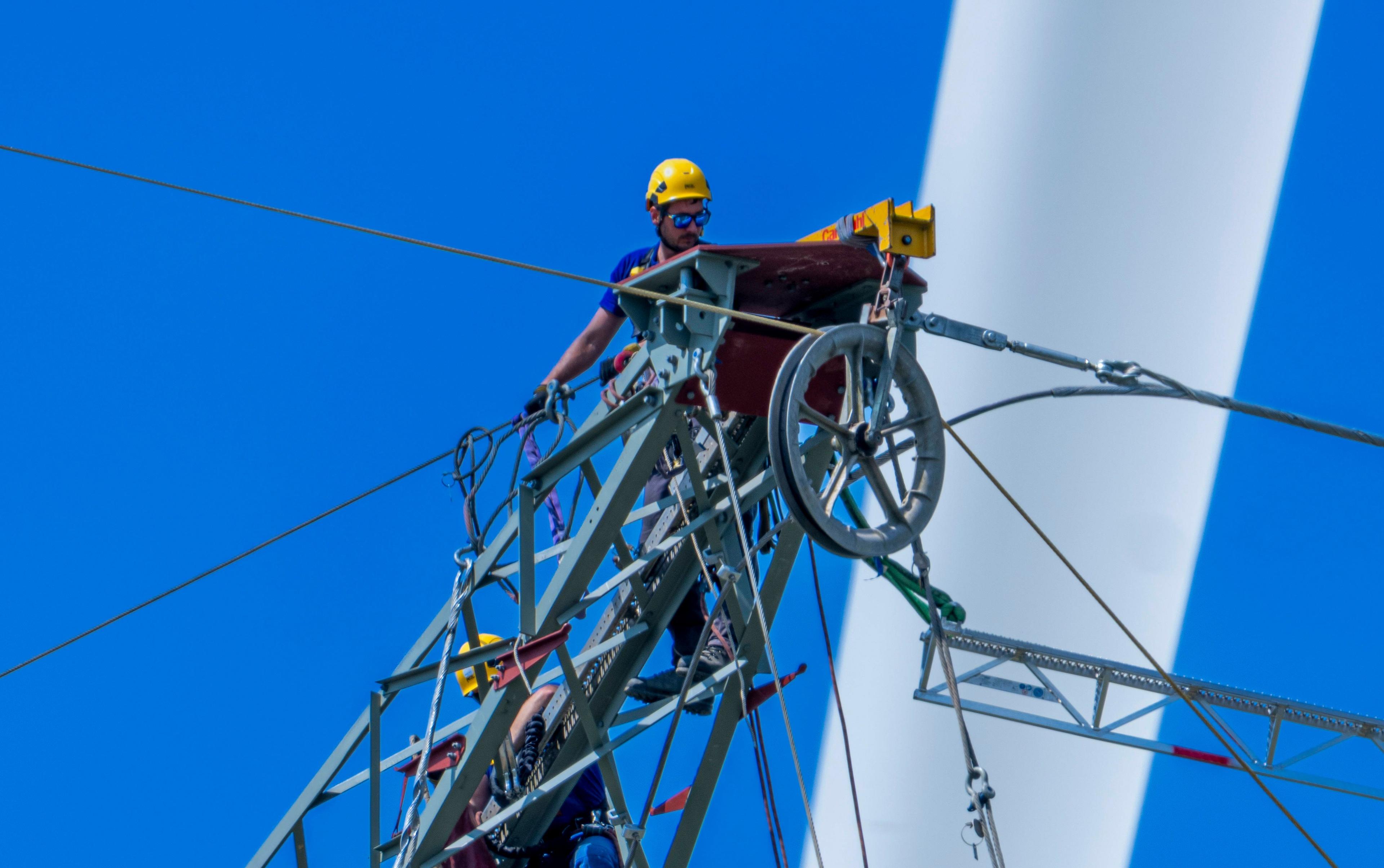Arbeiter auf einem Hochspannungsmast vor dem Rotorblatt eines Windrades bei Salzgitter.