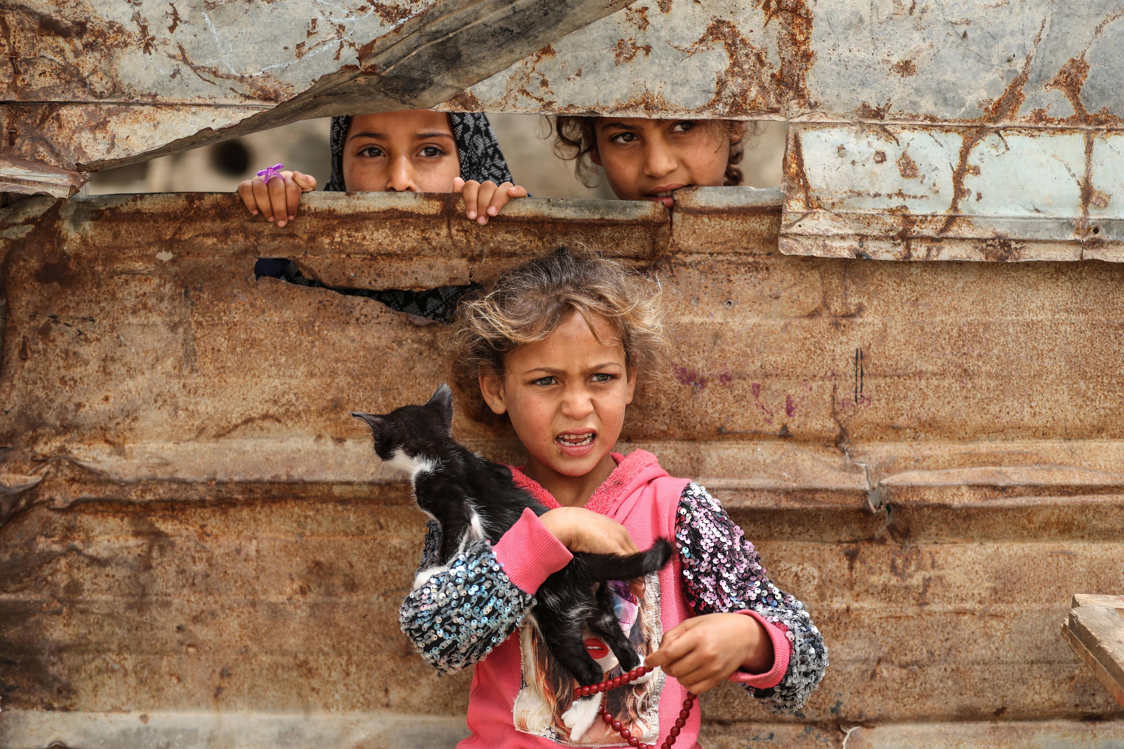 Kinder in Gaza blicken durch einen Spalt in einem Blechzaun, Aufnahme vom 24. April 2022.
